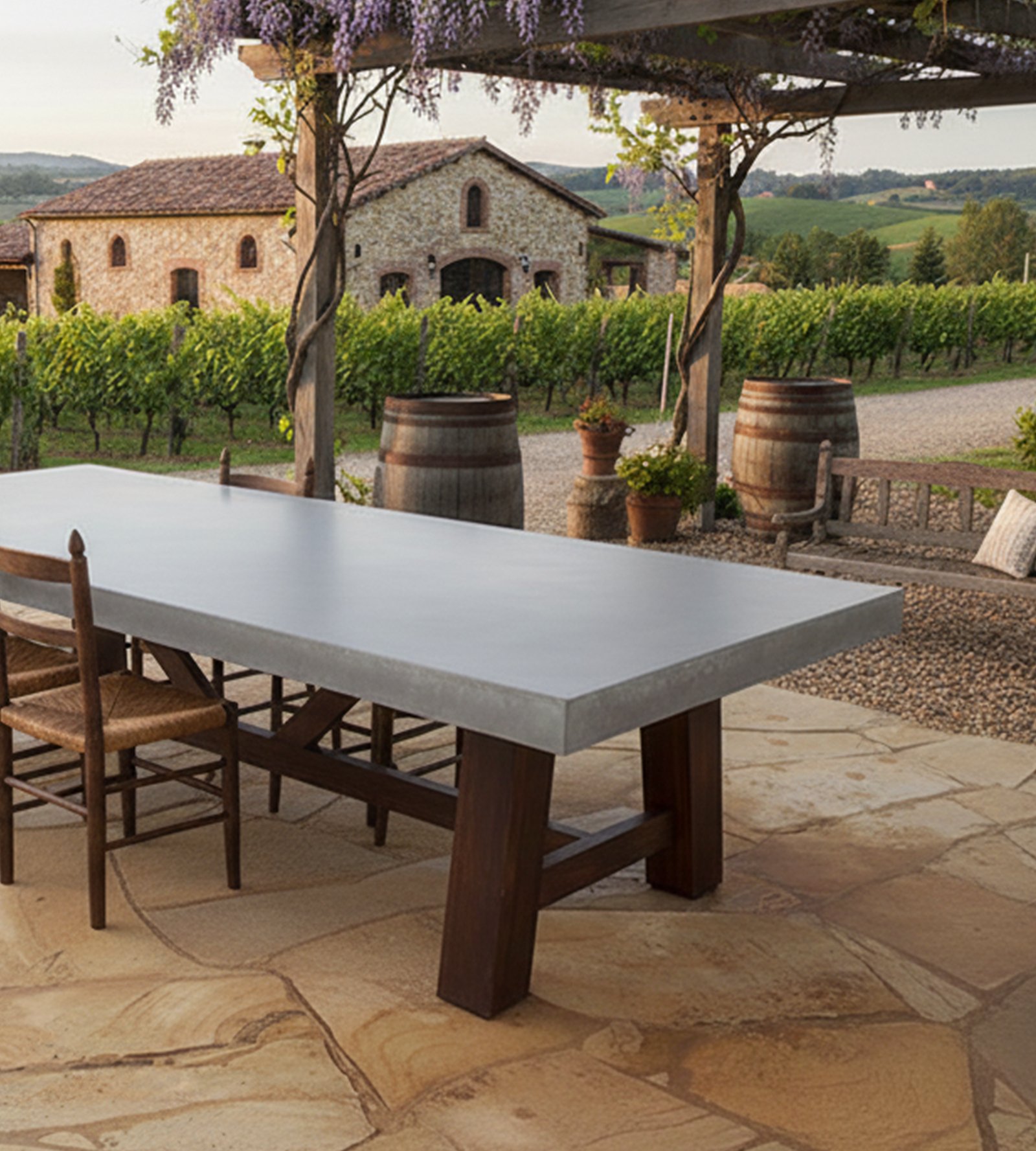 Farmhouse concrete dining table outdoors under a wisteria-covered pergola with Tuscan vineyard view