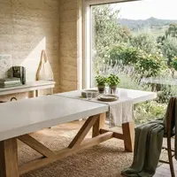 Farmhouse white concrete dining table in a rammed-earth Daylesford dining room with potted herbs, linen runner and an olive-and-lavender garden view