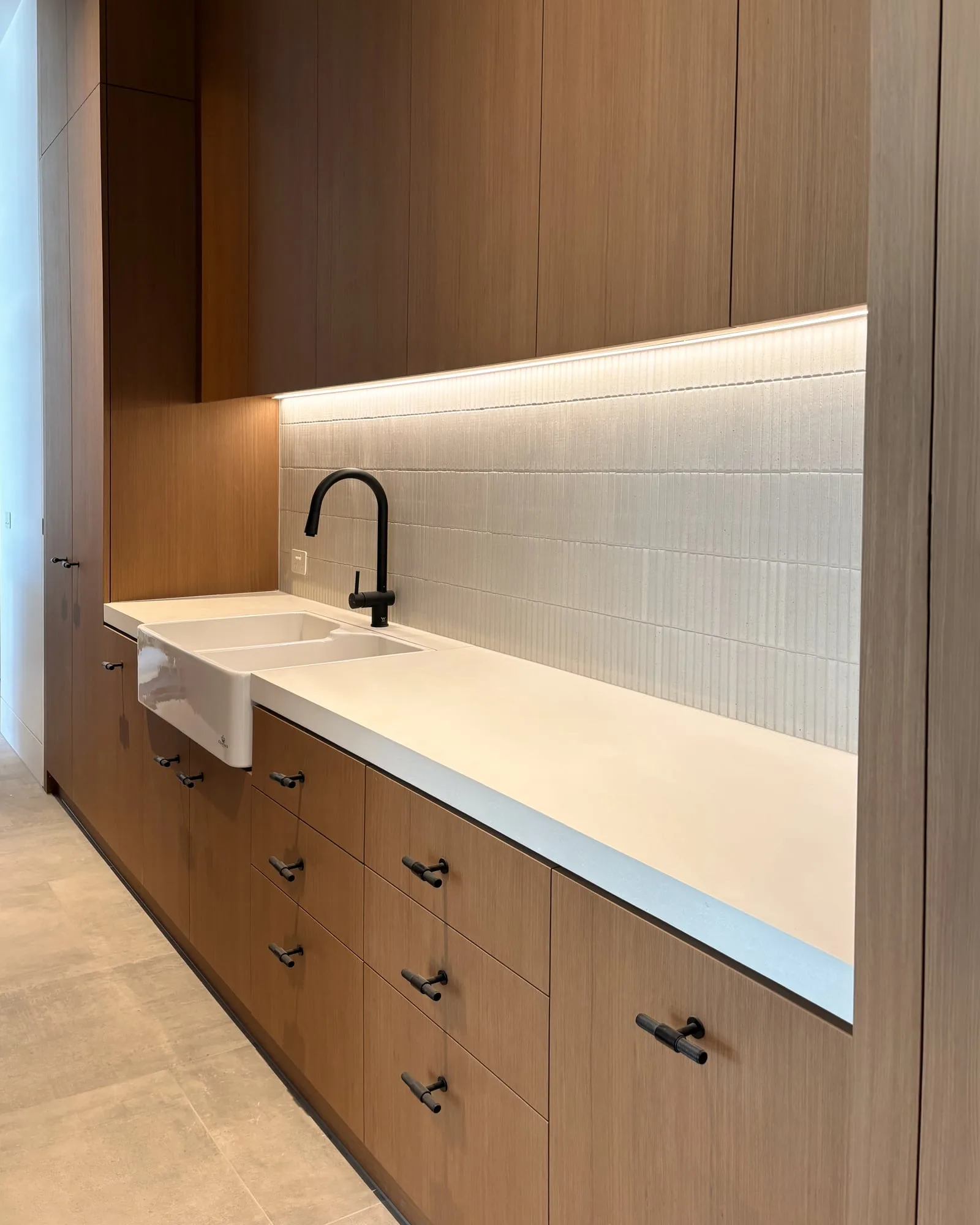A bone white concrete benchtop with a butler sink, ribbed white tile splashback and oak joinery, hand-cast by SnapCo
