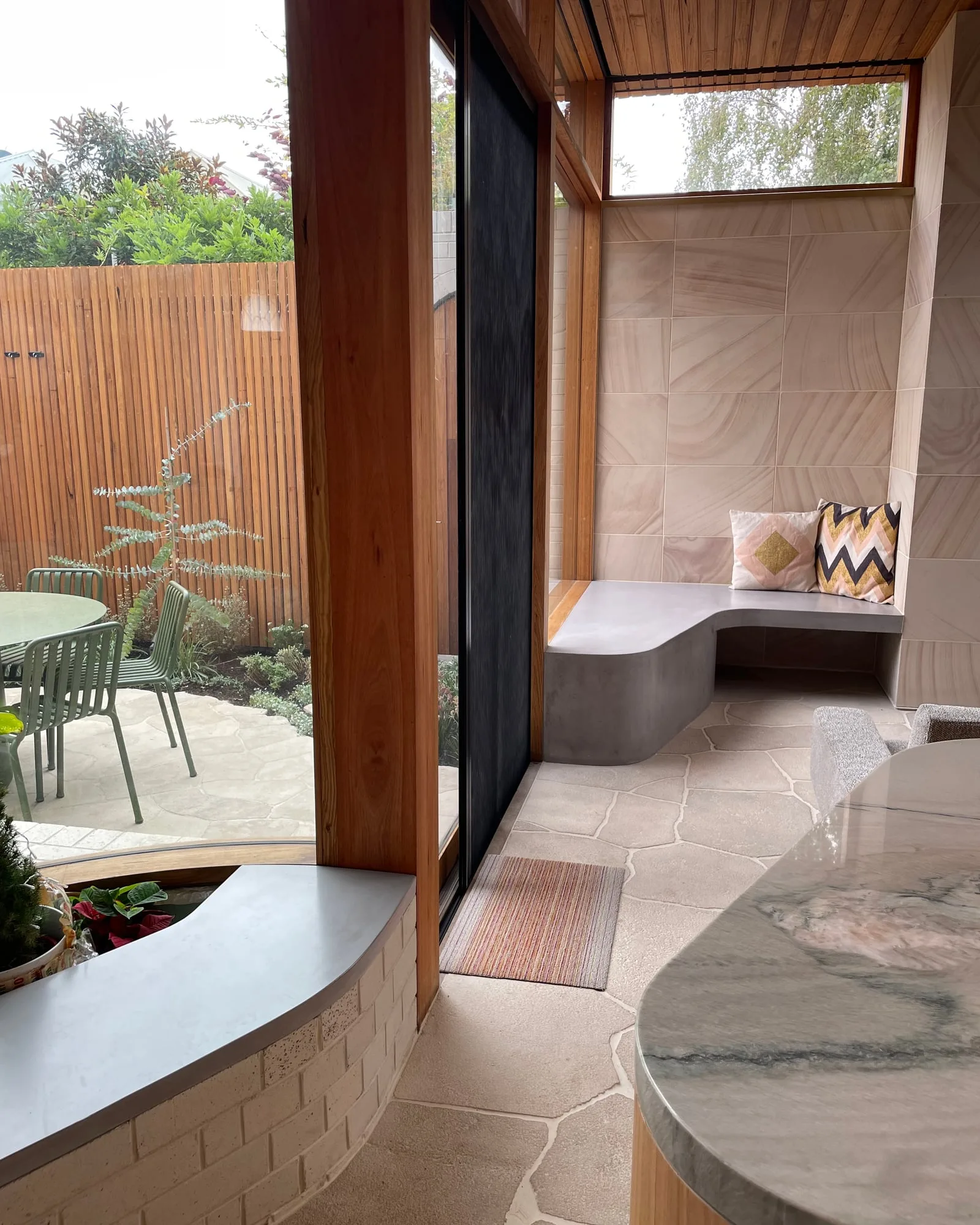 A custom concrete dining table in a residential interior with sandstone tile floor, oak timber framework and a built-in concrete banquette