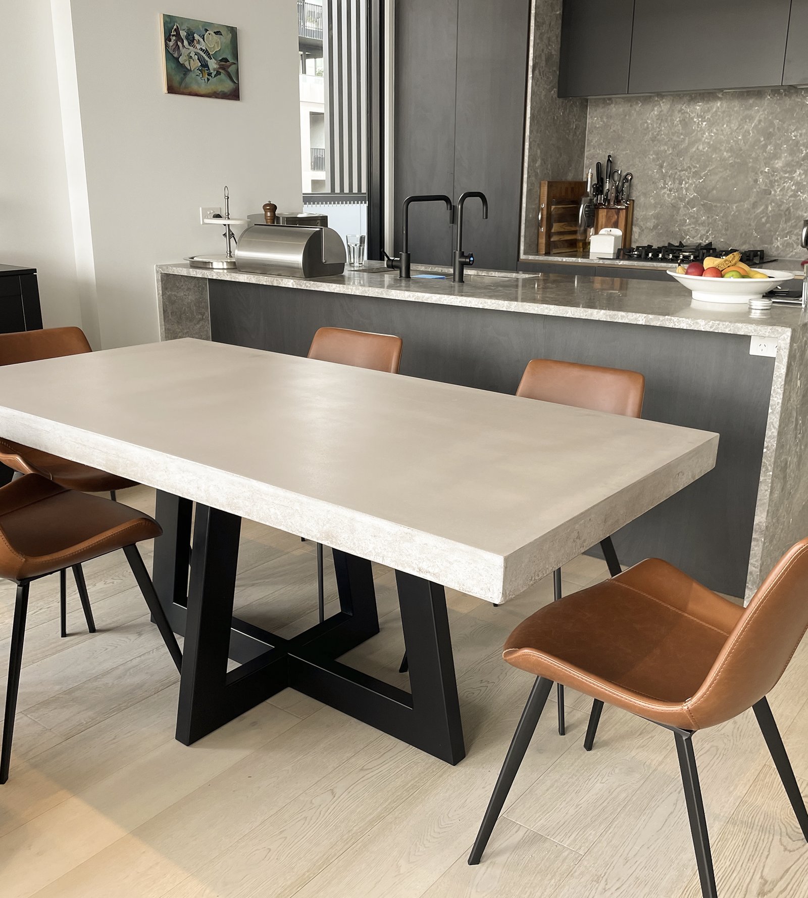 IronCross concrete dining table in a modern kitchen with tan leather chairs and grey marble island