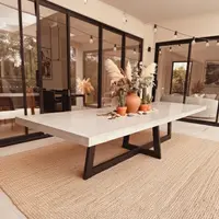 IronCross concrete dining table in a glass-walled room with pampas grass, terracotta urn and cacti styling on a jute rug