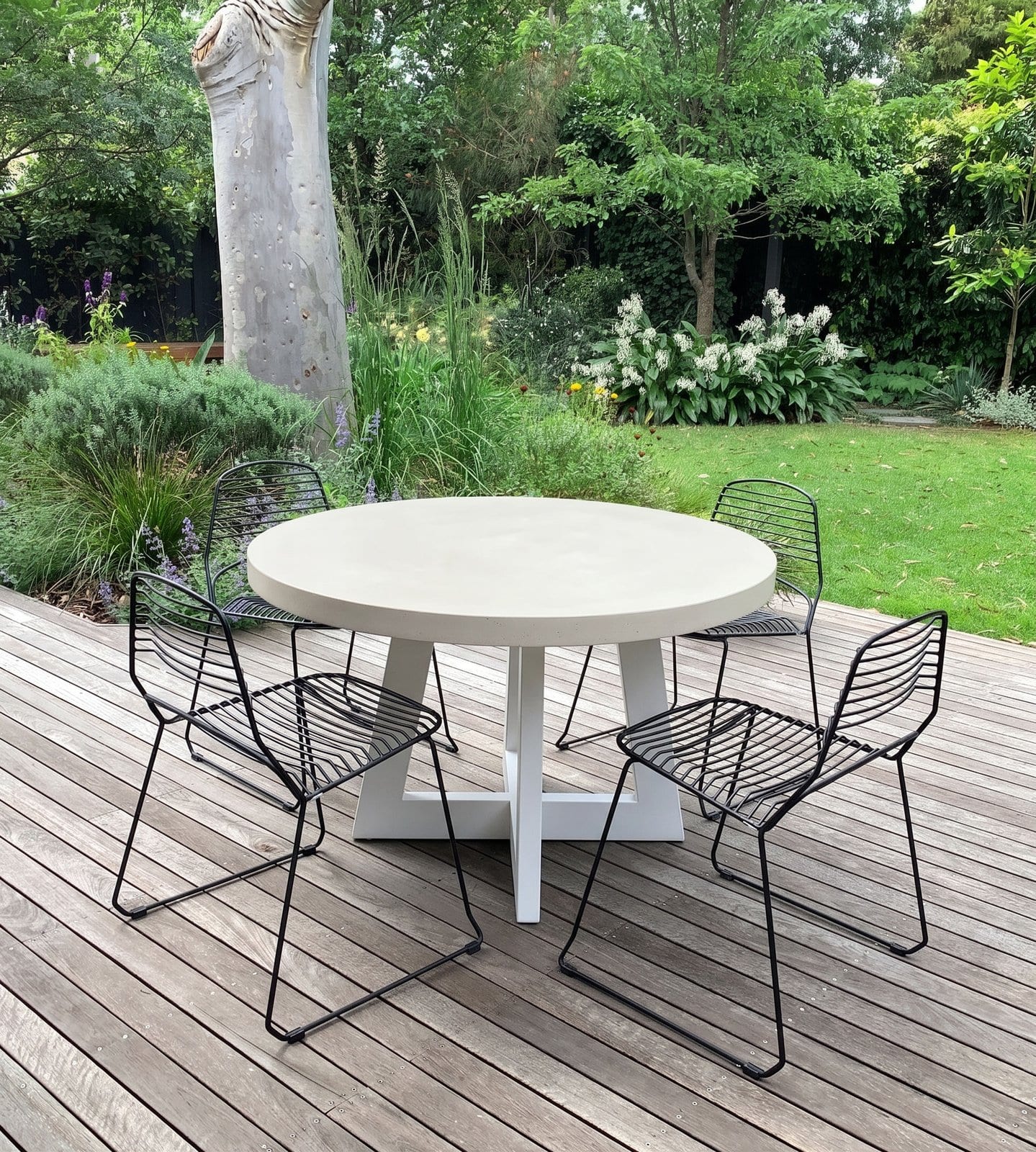 Close-up of the bone-white IronCross concrete dining table edge with stoneware jug and olive velvet chairs behind