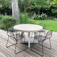 Close-up of the bone-white IronCross concrete dining table edge with stoneware jug and olive velvet chairs behind