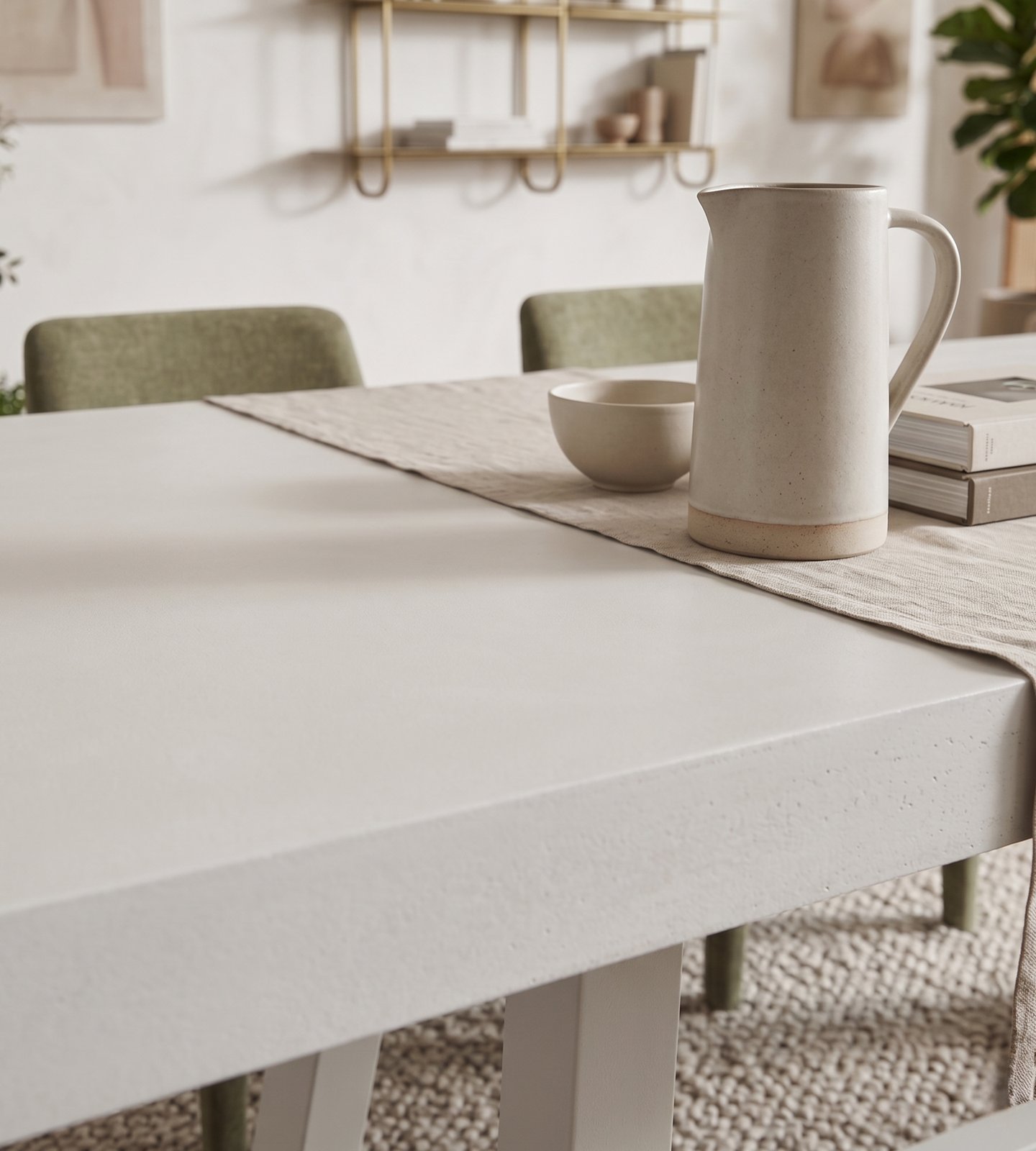 White IronCross concrete dining table in a light-filled interior with brass shelving, olive velvet chairs and fiddle-leaf fig