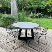 Round IronCross concrete dining table on a timber deck overlooking a lush cottage garden with black wire chairs