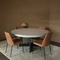 Round IronCross concrete dining table in a warm interior with four tan leather chairs and a paper-shade table lamp