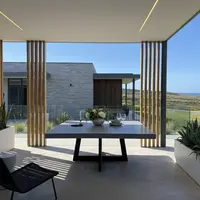 Square IronCross concrete dining table on a coastal patio with timber-batten screens, ocean view and agave planters