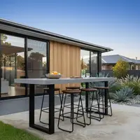 Outdoor IronStone concrete bar table with four black metal stools and timber seats at dusk