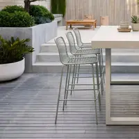 IronStone white concrete bar table on grey decking with sage-green wire bar stools and tropical planters