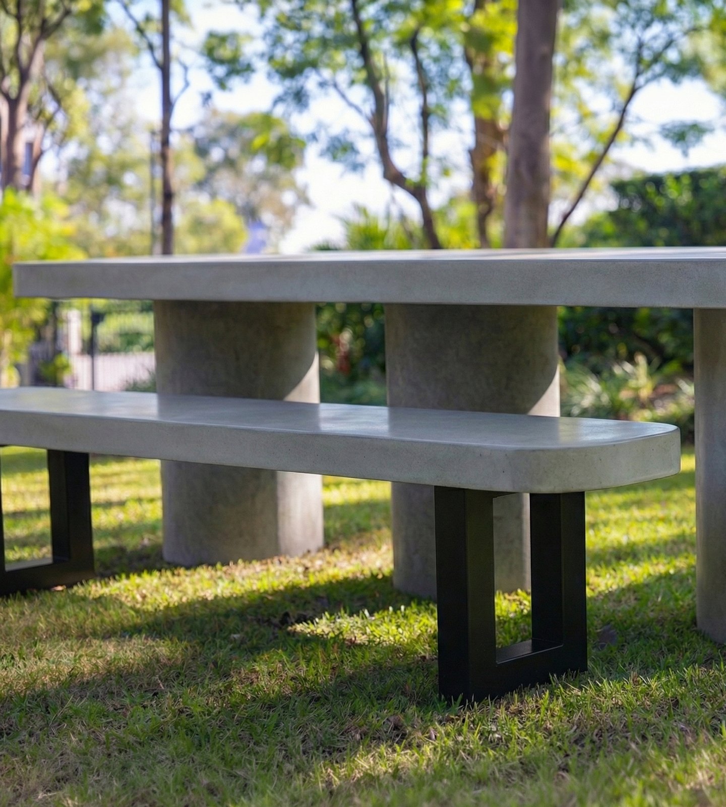 IronStone concrete bench seat on a sunlit lawn with eucalyptus trees behind, paired with a round concrete-column table