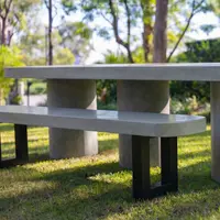 IronStone concrete bench seat on a sunlit lawn with eucalyptus trees behind, paired with a round concrete-column table