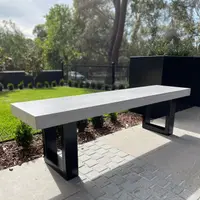IronStone concrete bench seat with black steel sled legs on pavers, beside a manicured garden with hedge and lawn