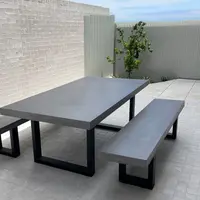 IronStone concrete dining table and bench seat on a tiled outdoor patio with white brick wall and Japanese maple