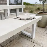 Close-up of a white IronStone concrete bench on a beach-house flagstone patio with olive tree in a stoneware pot