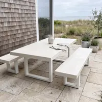 White IronStone concrete dining table and bench seat on a beach-house flagstone patio with shingle wall and olive trees