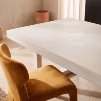 Close-up of the bone-white IronStone concrete dining table edge with white steel sled leg and mustard velvet chair