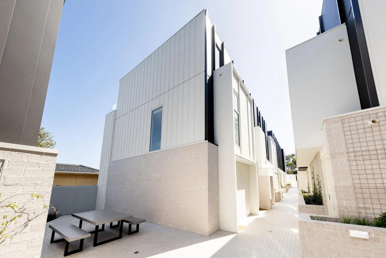 Exterior street view of the 93 Earl Street Kew multi-residential development designed by Cera Stribley, three levels of dark-clad apartments above a white-brick perimeter wall and landscaped front garden, where SnapCo concrete bench seats anchor the communal entertaining areas behind