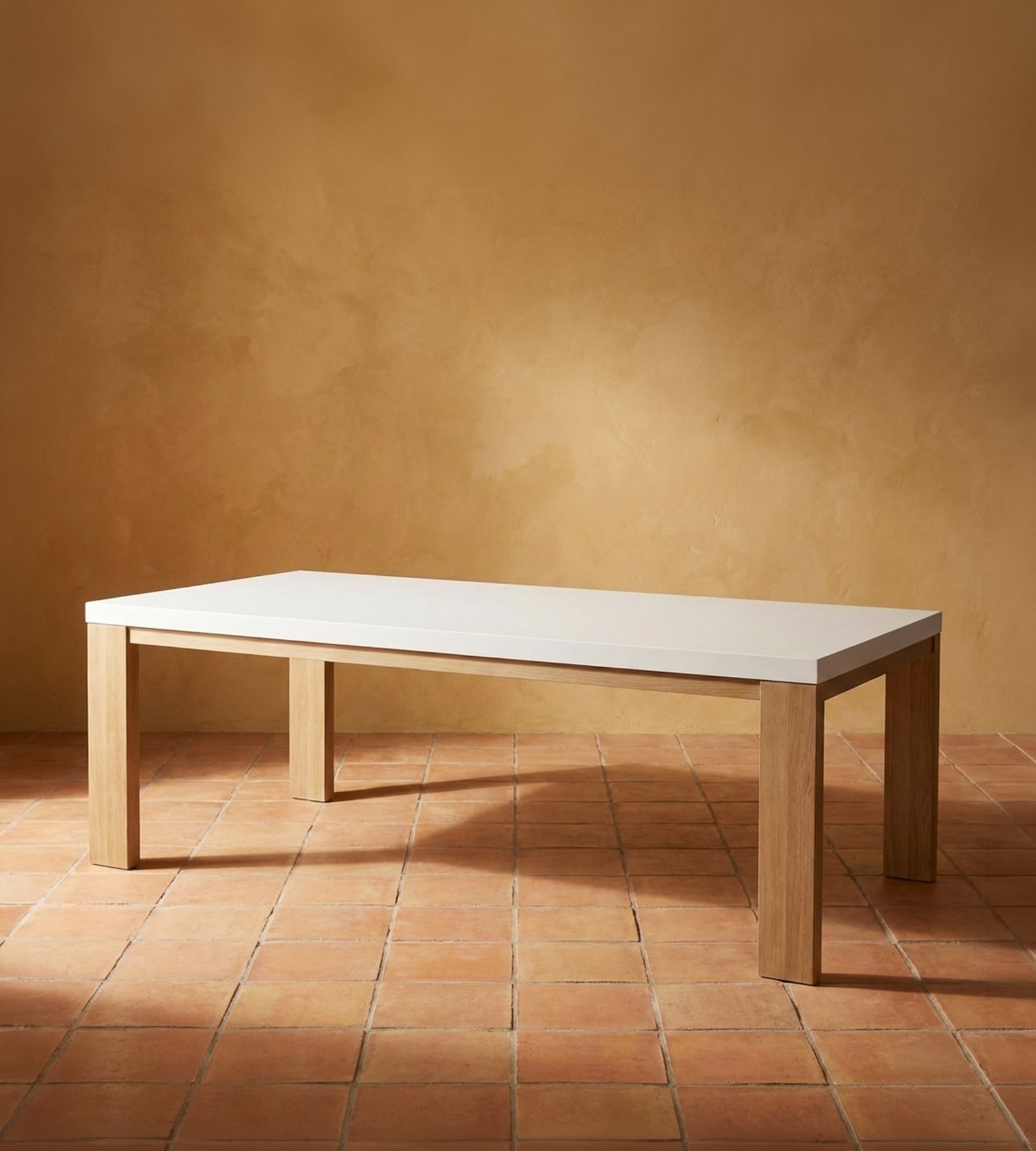 Laconian concrete dining table with white top and oak legs on terracotta tile against a warm ochre plaster wall
