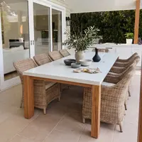 Laconian concrete dining table with white top and oak base on an undercover stone patio with wicker chairs and olive branches