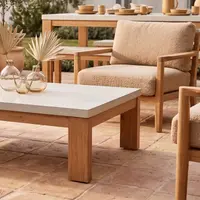Laconian concrete coffee table close-up with boucle armchair and dried palms in glass vases on a terracotta-tiled patio