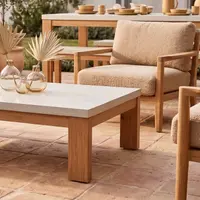 Laconian white concrete coffee table close-up with boucle armchair and dried palms in glass vases on a terracotta-tiled patio