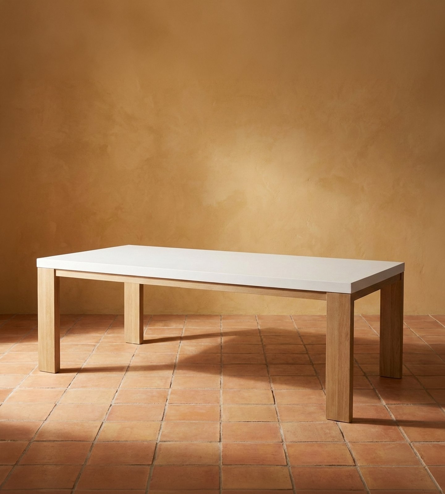 Laconian white concrete dining table with natural oak legs on terracotta tile against a warm ochre plaster wall