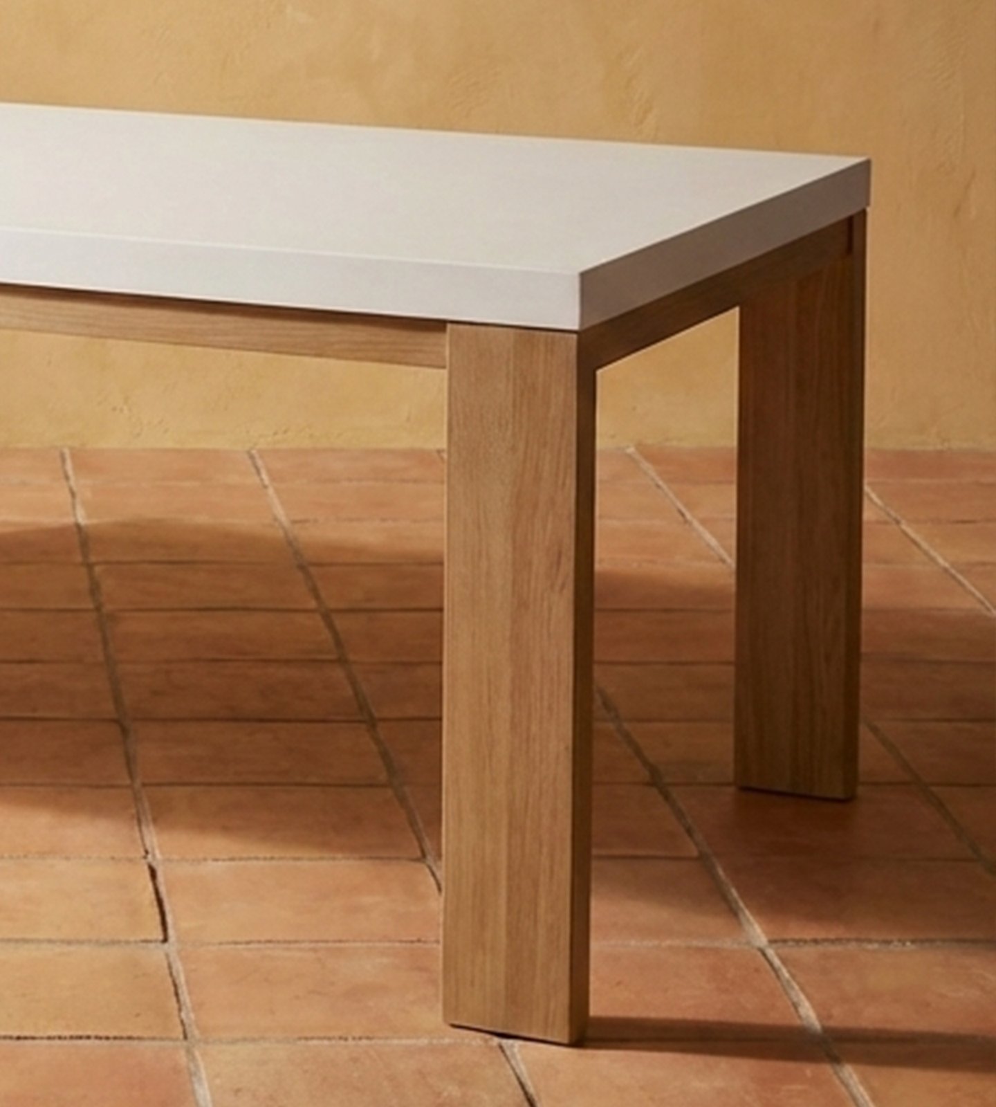 Close-up corner detail of the Laconian white concrete dining table showing the oak leg-to-top join on terracotta tile