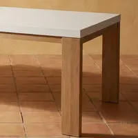 Close-up corner detail of the Laconian white concrete dining table showing the oak leg-to-top join on terracotta tile