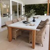Laconian white concrete dining table with oak legs set under a vaulted skylight veranda, wicker armchairs, olive branch centrepiece