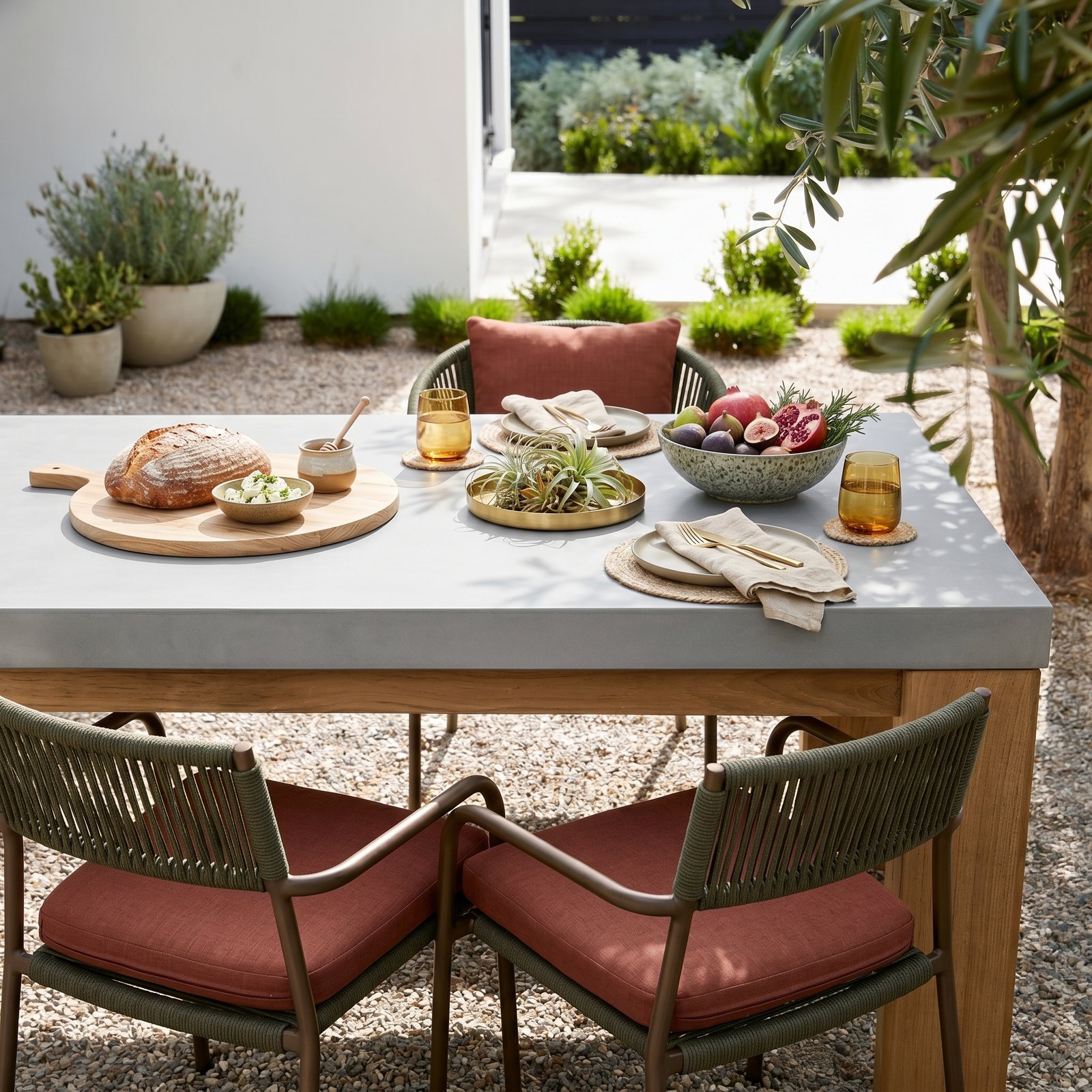 Laconian concrete dining table styled with bread, fruit, and brass tableware in a Mediterranean garden