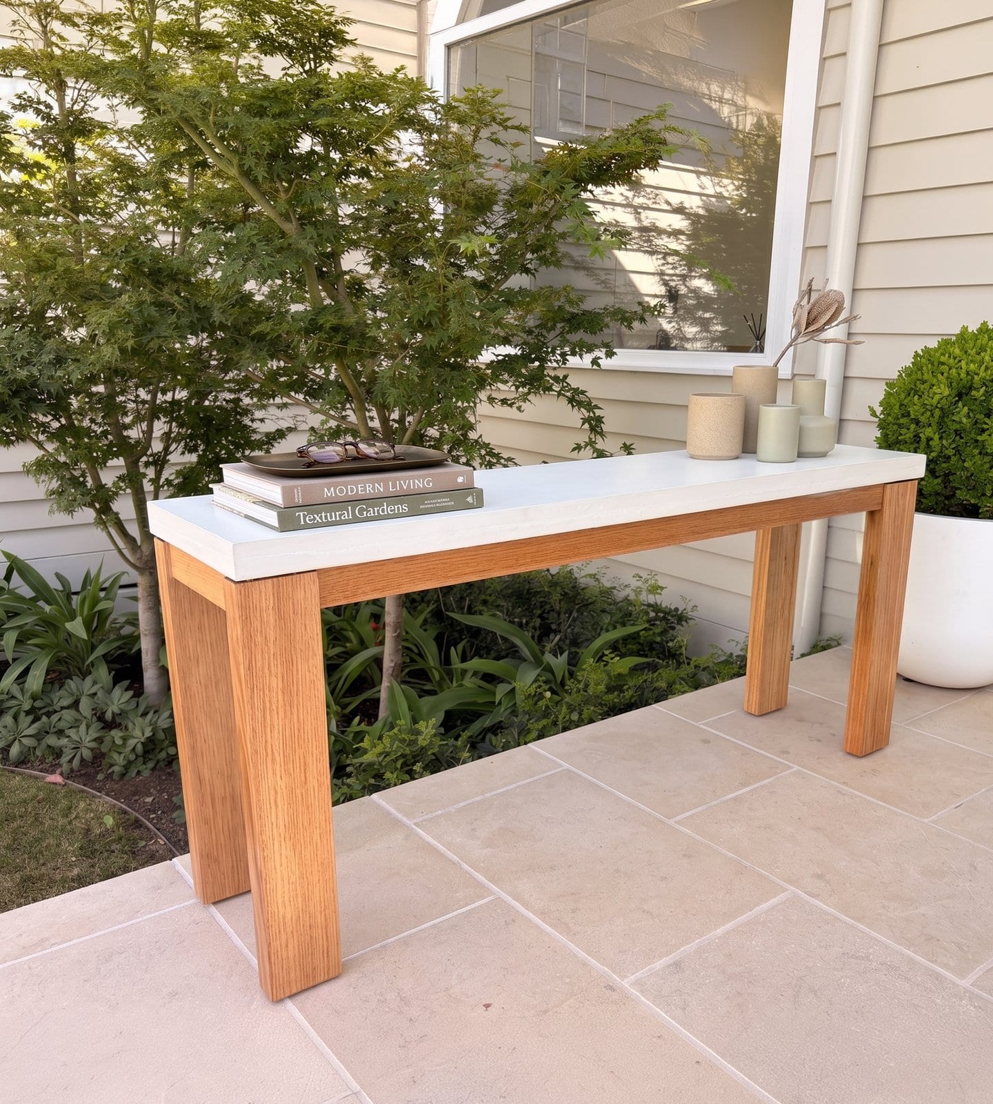 Laconian concrete hall table styled outdoors with garden books, glasses and stoneware vessels