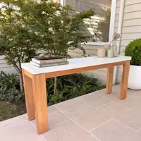Laconian white concrete hall table on a paved patio with a Japanese maple, design books, ceramic candles and a clipped buxus