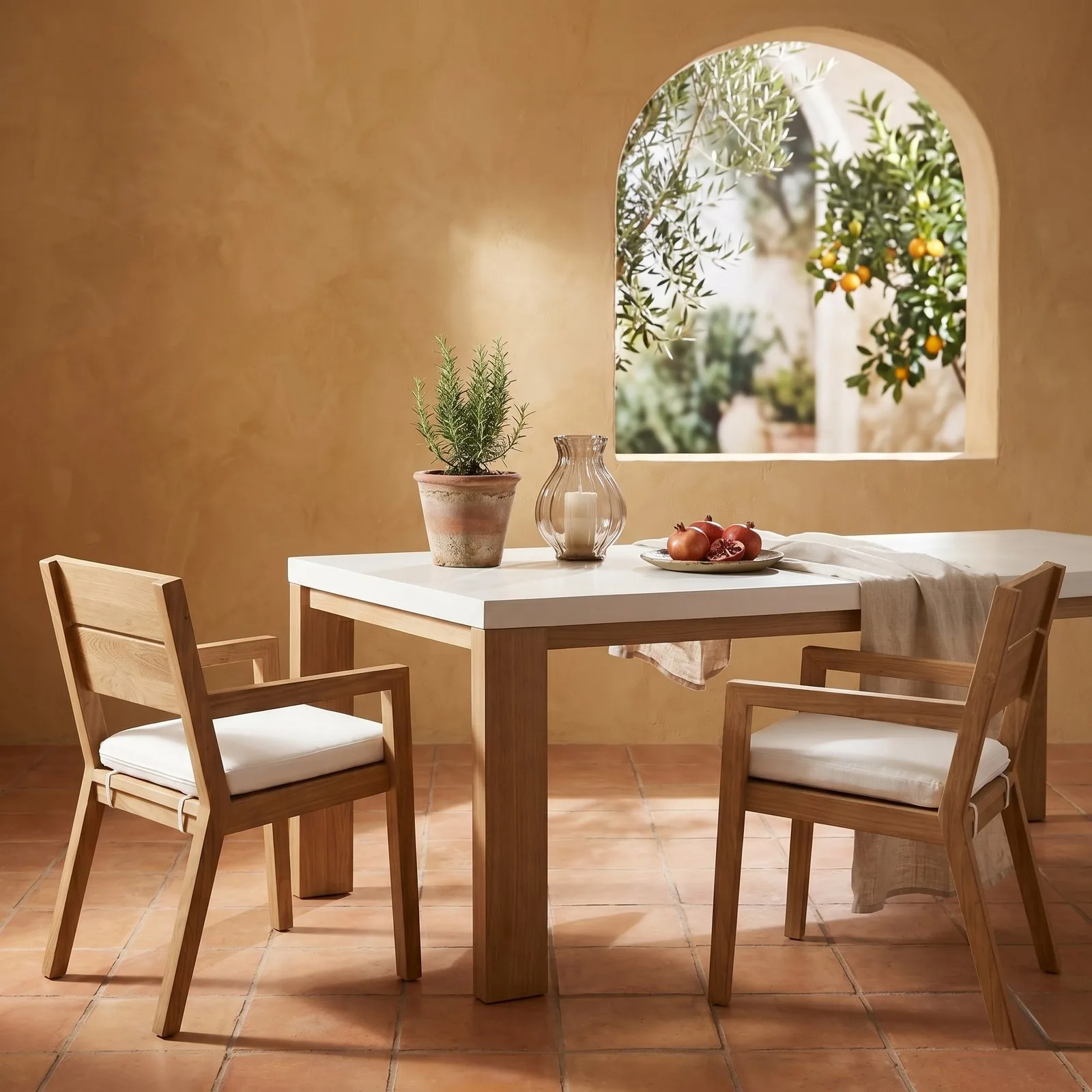 Laconian concrete dining table with bone-white top in a Mediterranean room with arched window onto olive and citrus trees