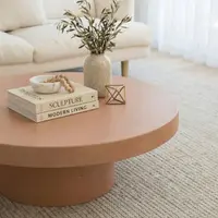 Milano round terracotta concrete coffee table close-up with books and olive branches in front of a cream sofa
