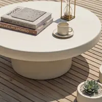 Milano white concrete coffee table on timber decking with stacked travel books, brass hourglass, espresso cup and succulent planter, overhead view