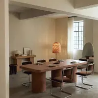 Milano rectangular concrete dining table in desert red pigment, with cantilever chairs and rattan lamp in a warm plaster-walled dining room