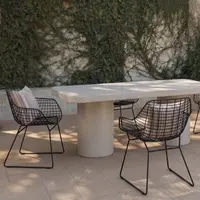 Milano rectangular white concrete dining table on twin cylindrical concrete pedestals in a sunlit Mediterranean courtyard with black wire armchairs, striped cushions and an ivy-clad plaster wall