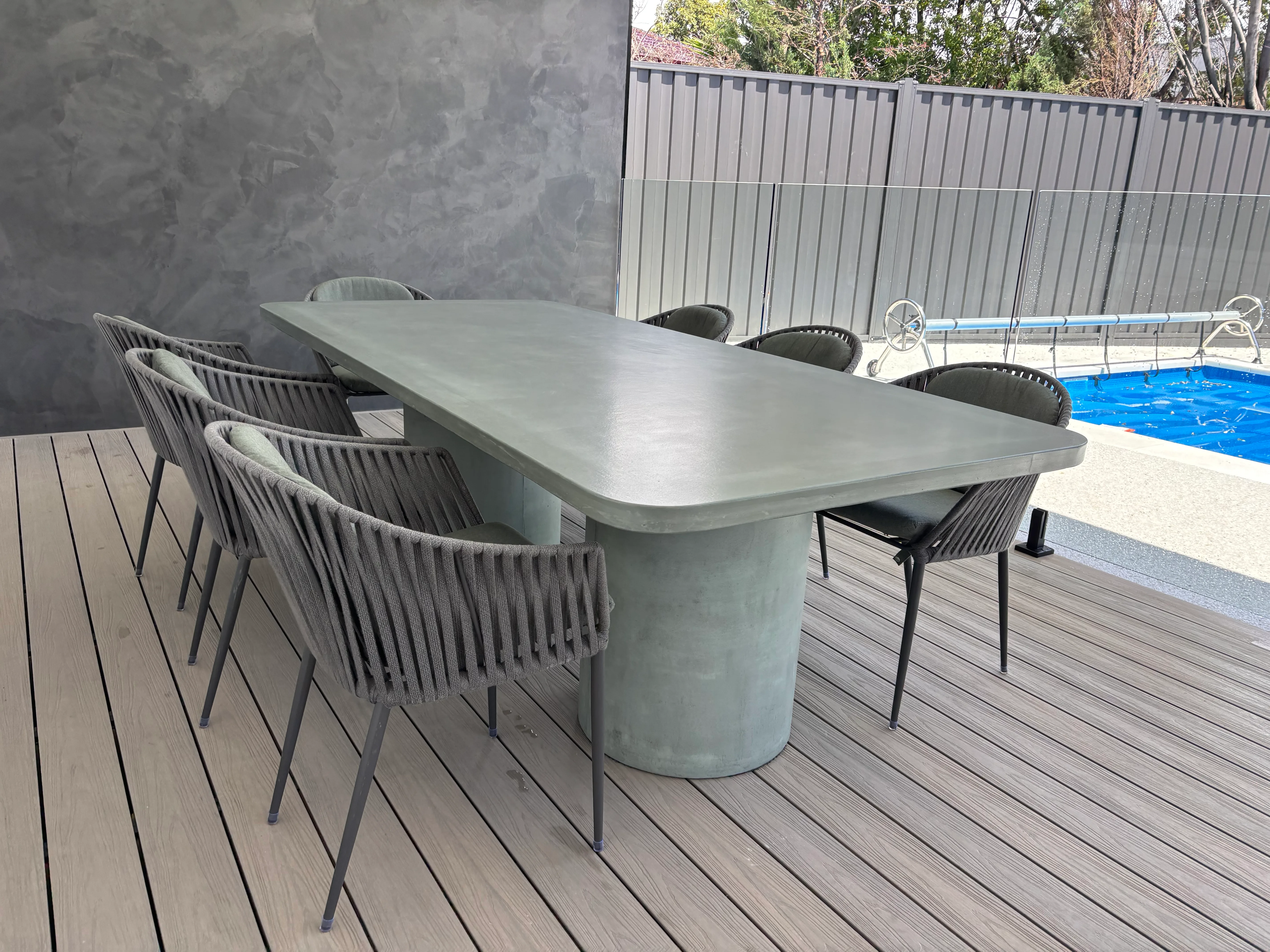 Sage Milano rectangular concrete dining table outdoors with round concrete-leg pedestals and rope-back dining chairs