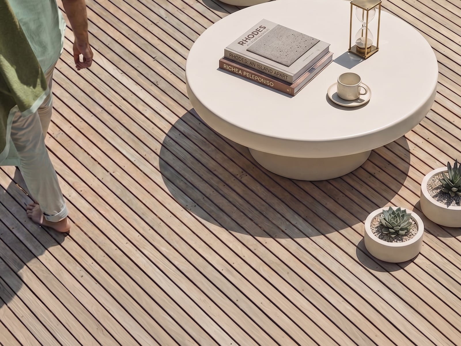 Bone white concrete outdoor coffee table on a sunlit timber deck, styled with a stack of books, a stoneware mug and brass hourglass