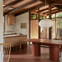 Terracotta Palermo oval concrete dining table in a mid-century home with timber-beam ceiling and red brick floor