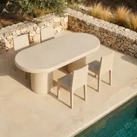Palermo oval concrete dining table on a Mediterranean poolside terrace, parsons chairs and stacked-stone retaining wall with olive tree and golden grasses