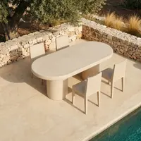 Palermo bone white concrete oval dining table on a Mediterranean poolside terrace, sage parsons chairs, stacked-stone retaining wall, mature olive tree and golden grasses