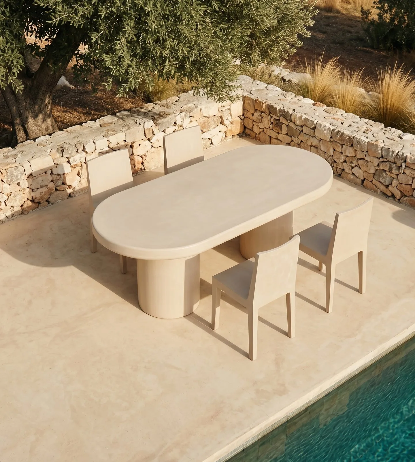 Palermo bone white concrete oval dining table on a Mediterranean poolside terrace, sage parsons chairs, stacked-stone retaining wall, mature olive tree and golden grasses