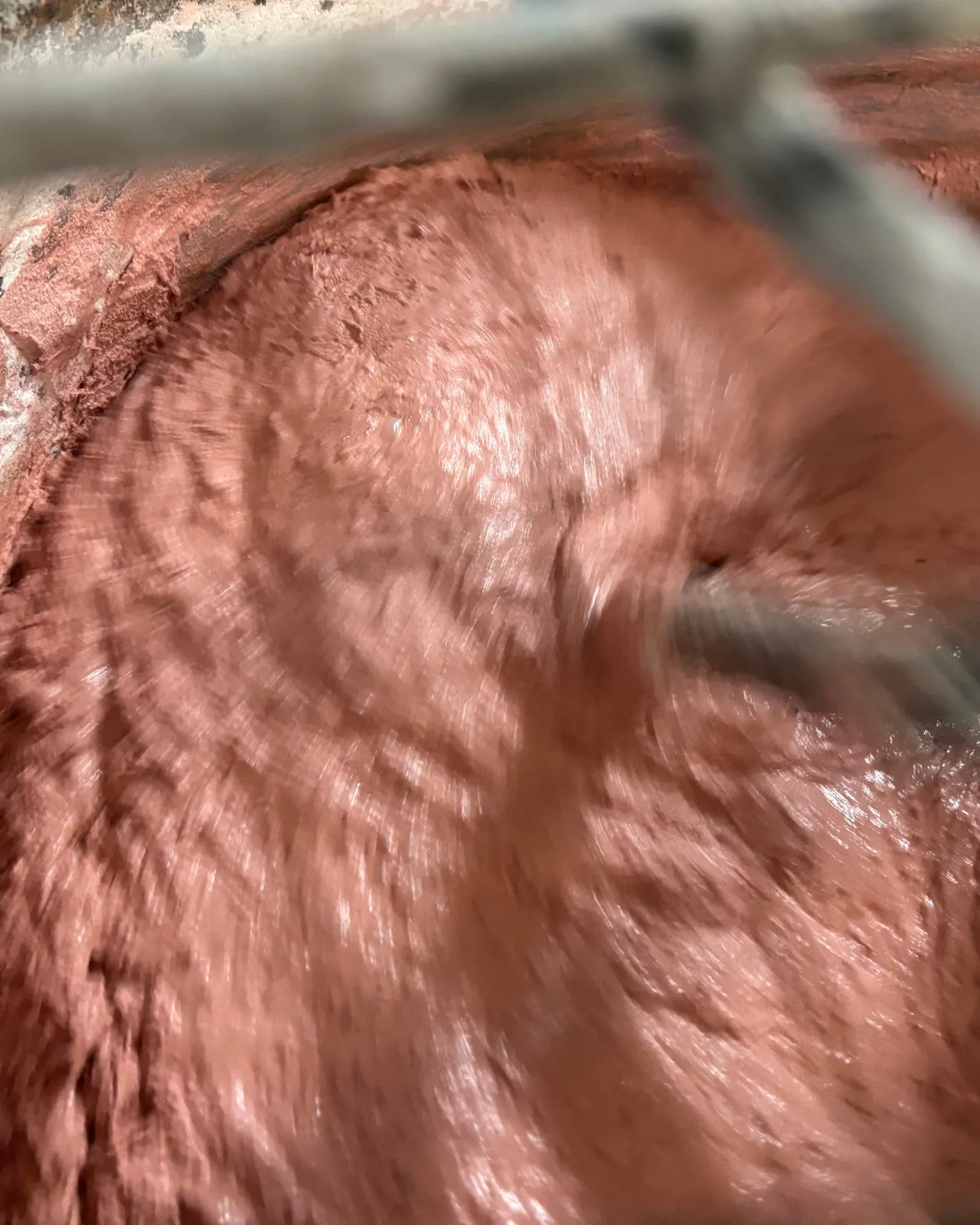 Red iron-oxide pigment being mixed through wet concrete in the SnapCo Mordialloc studio mixer, showing the colour saturating the full composition