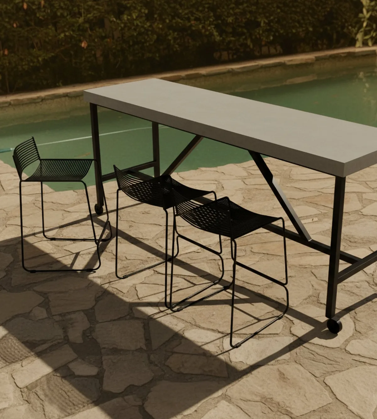 Santino concrete bar table by a pool with black wire bar stools on a flagstone terrace