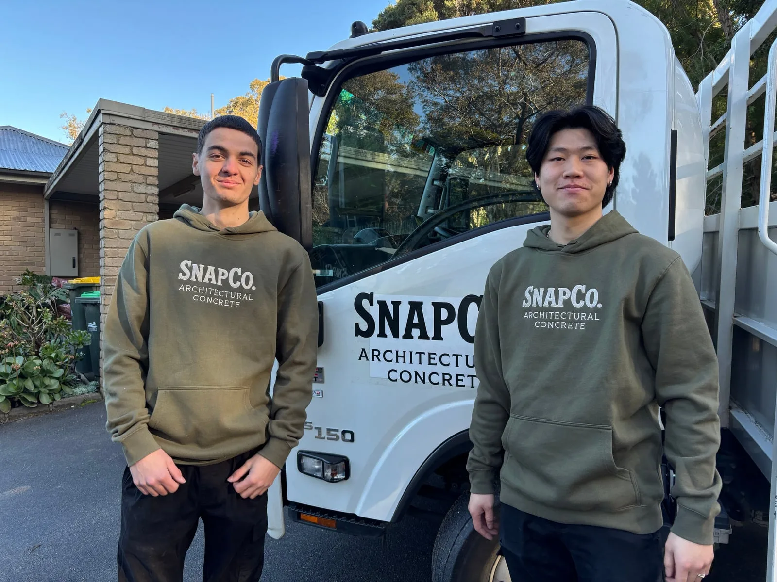 Two members of the SnapCo casting and delivery team in olive SnapCo Architectural Concrete hoodies, standing in front of the studio truck at the Mordialloc workshop