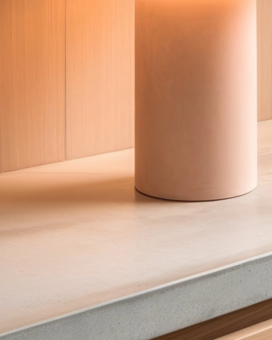 A pigmented concrete table lamp on a concrete benchtop in a warm timber kitchen