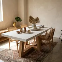 TimberCross concrete dining table styled with cane chairs, dried palm fronds, ceramic bowls and a Persian rug in a sunlit dining room