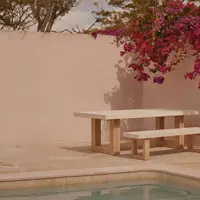 TimberStone concrete bench seat in Bone White on a sandstone pool terrace with bougainvillea overhead and pink plaster wall